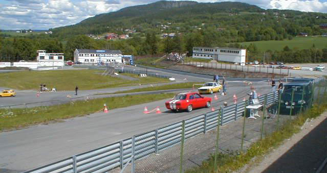 Mye skjedde samtidig på Lyngåsbanen. På banen nærmest (Bane 2) ser vi Eivind Løland i sin røde Opel Kadett. Klar til start står Kadetten til Anre Manger. På nederste bane (Bane 1) ser vi Kjartan Hjørnevik feie rundt banen.